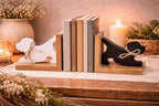 A pair of dog-shaped bookends on a wooden table, holding a set of books. One bookend is white with a jute bow, and the other is black with a jute bow.
