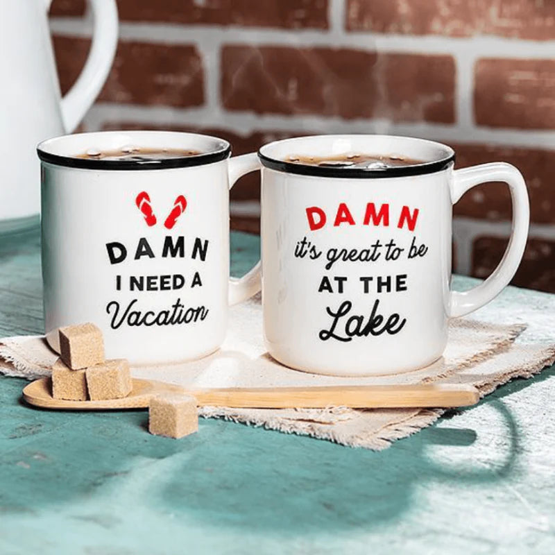 Two mugs with humorous text on a table with a brick wall background