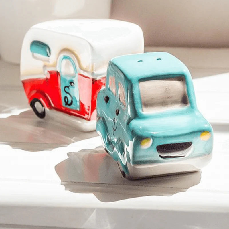 Ceramic car and camper salt and pepper shaker, one blue and one multicoloured, on a reflective surface.