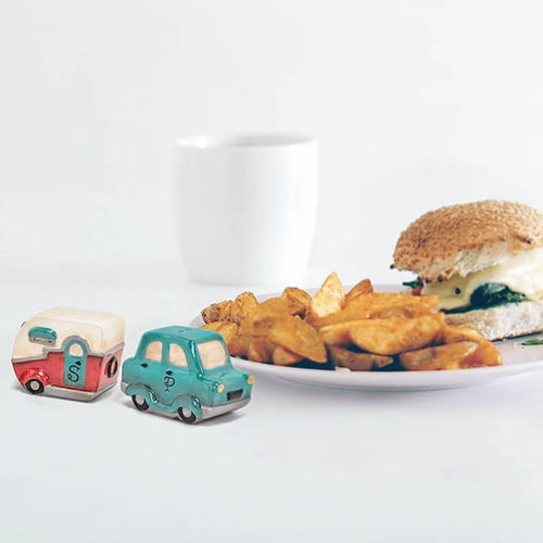 Two novelty salt and pepper shakers shaped like a camper and a car on a table with a plate of food.