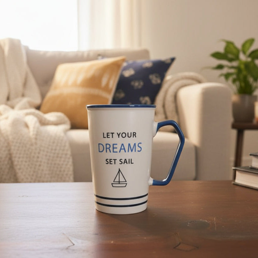 White mug with blue handle and text 'Let your dreams set sail' on a wooden surface.
