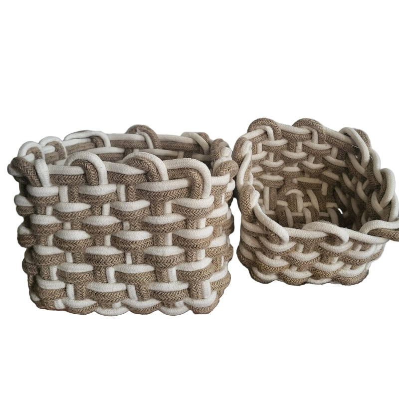 Two woven storage baskets with a braided jute and white rope pattern, displayed on a wooden chest against a white wall.